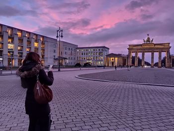 Rear view of women standing on footpath in city against sky