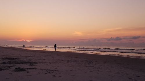 Distant view of silhouette person running at beach during sunset