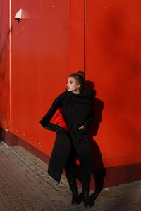 Woman looking away while standing against red wall