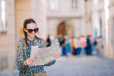 Portrait of young woman holding map while standing in city