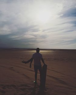 Rear view of man with surfboard standing at beach during sunset