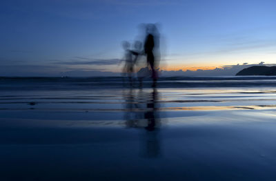 Blurred motion of silhouette people at beach against sky during sunset