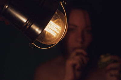 Close-up portrait of woman by illuminated light bulb