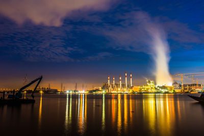 Illuminated city by river against sky at night