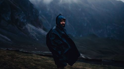 Portrait of man wearing a poncho in a raining morning with mountain range in the background