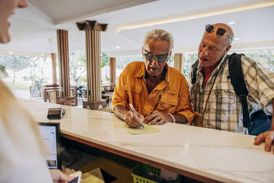 Senior gay couple filling form at reception desk in hotel