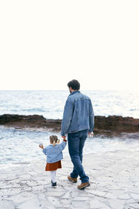 Rear view of father and daughter walking near sea