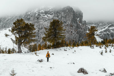 Rear view of female hiker walking on snowy path under amazing misty mountains