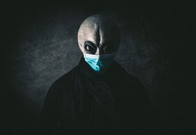 Portrait of alien wearing mask against black background