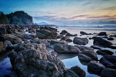 Rocks on beach against sky during sunset