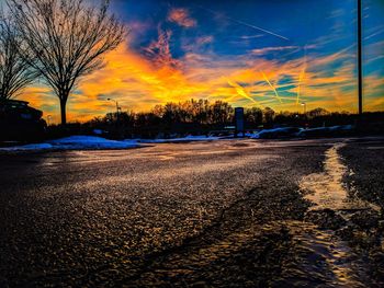 Road by bare trees against sky during sunset