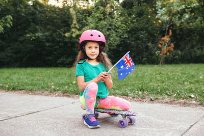 Portrait of smiling girl holding australian flag sitting on skateboard