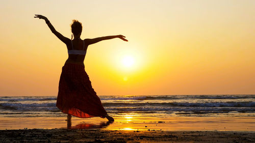 Rear view of woman practicing yoga at beach during sunset