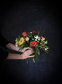 Midsection of woman holding flower bouquet against black background