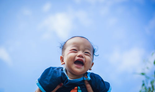 Cropped image of mother picking up baby against sky