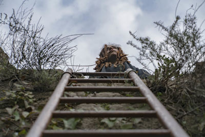 Low angle view of ladder leading towards woman against sky