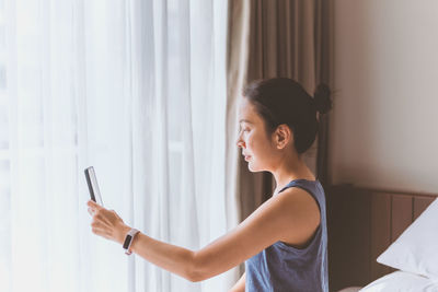 Side view of young woman using mobile phone at home