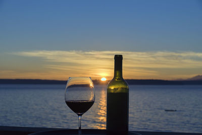 Close-up of wineglass and bottle against sea during sunset