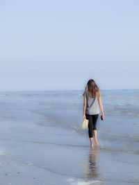 Rear view of woman standing on beach against clear sky