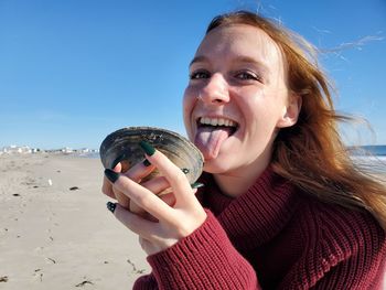 Portrait of smiling woman holding seashell against sky