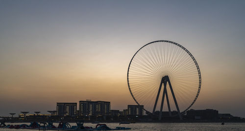 Ferris wheel by sea against sky during sunset