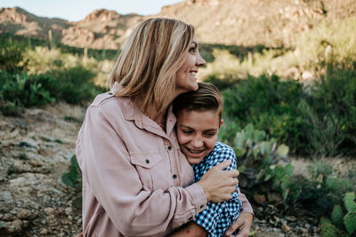 Mother hugging smiling non binary child in the desert