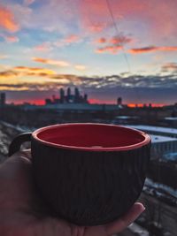 Close-up of hand holding drink against sky during sunset