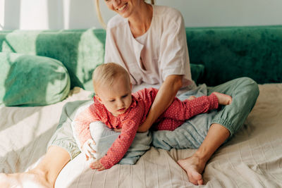 Midsection of mother and daughter lying on bed at home