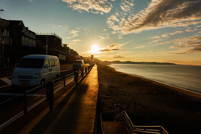 Cars on street by sea against sky during sunrise 