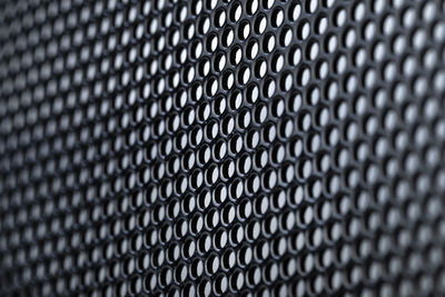 Macro shot of a black metal surface with round holes, gray background.