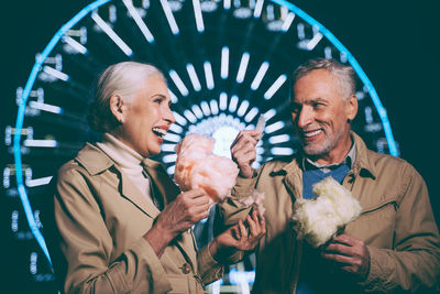 Smiling couple eating cotton candy while standing at carnival