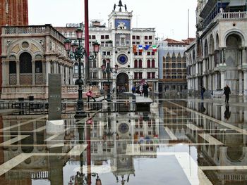 Historical building reflecting on wet footpath in city