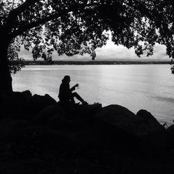 Silhouette of man sitting on beach against sky