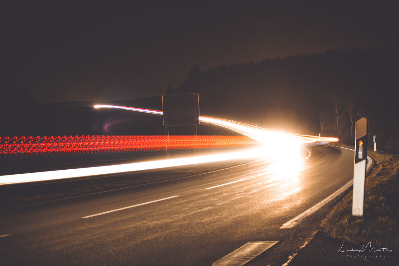 LIGHT TRAILS ON ROAD AGAINST SKY AT NIGHT