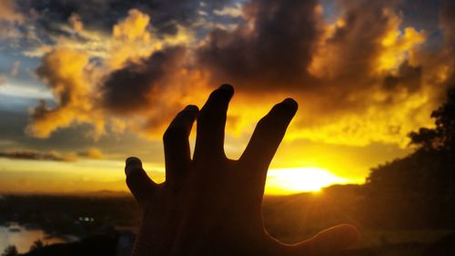 Silhouette hand against sky during sunset