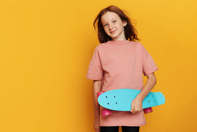 Portrait of young woman standing against yellow background