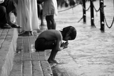 Full length side view of shirtless girl praying while bathing at riverbank