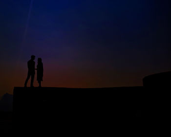 Silhouette couple standing against sky at dusk