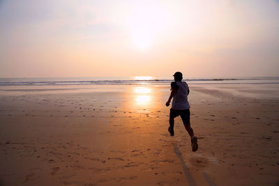 Rear view of man on beach against sky during sunset