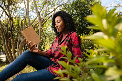 Young woman sitting on plant against trees