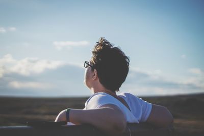 Side view of woman sitting on bench against sky