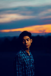 Man looking down while standing against sky during sunset