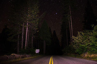 Road amidst trees in forest against sky at night