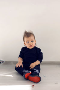 Baby sitting on the floor with red sole sneakers