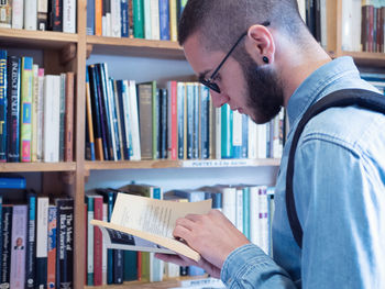 Side view of man reading book in library