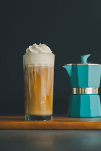 Ice cappuccino with whipping cream on a wooden table with a black background and green moka pot. 