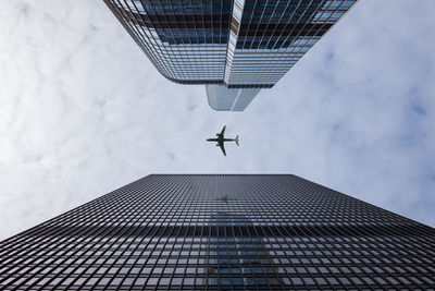 Low angle view of airplane flying over building against sky
