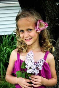 Portrait of smiling girl holding flowers while standing against plants