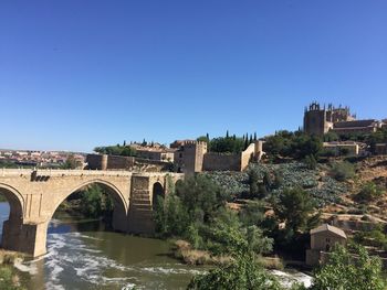 Bridge over river in city against clear sky