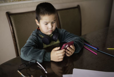 Portrait of boy looks in phone sitting on floor, playing on phone instead of drawing with pencils